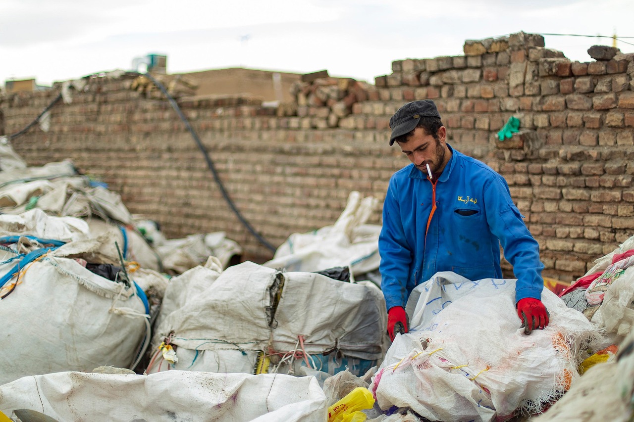 Sanitation workers loading garbage into a waste collection truck, representing labor costs in waste management operations.